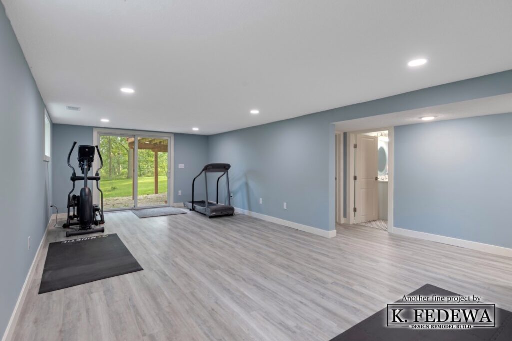 A workout area in a Williamston, MI basement remodel with a light grey vinyl floor, light blue walls, white ceiling, sliding door, and exercise equipment.
