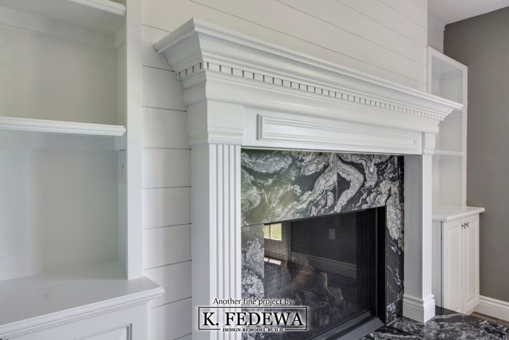 Large fireplace with black granite surround, white mantel, and white built-in shelving on both sides.