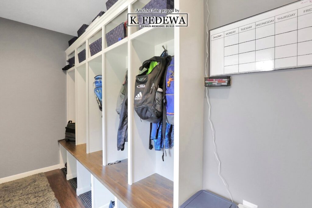Mudroom with white cubbies that have coats and backpacks hanging in them with a wooden bench for people to sit.