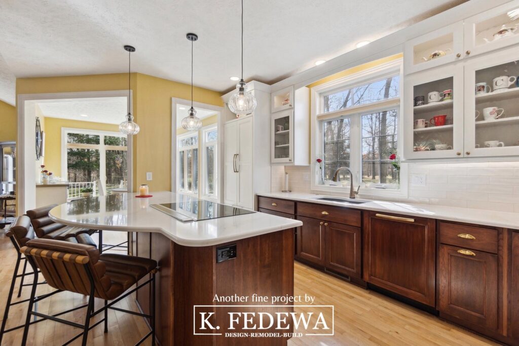 Incredible Bath, MI Kitchen Remodel from K. Fedewa Builders with dark wood cabinets on the bottom, white upper cabinets, a white countertop, light wood flooring, and stools on the left at a large island.
