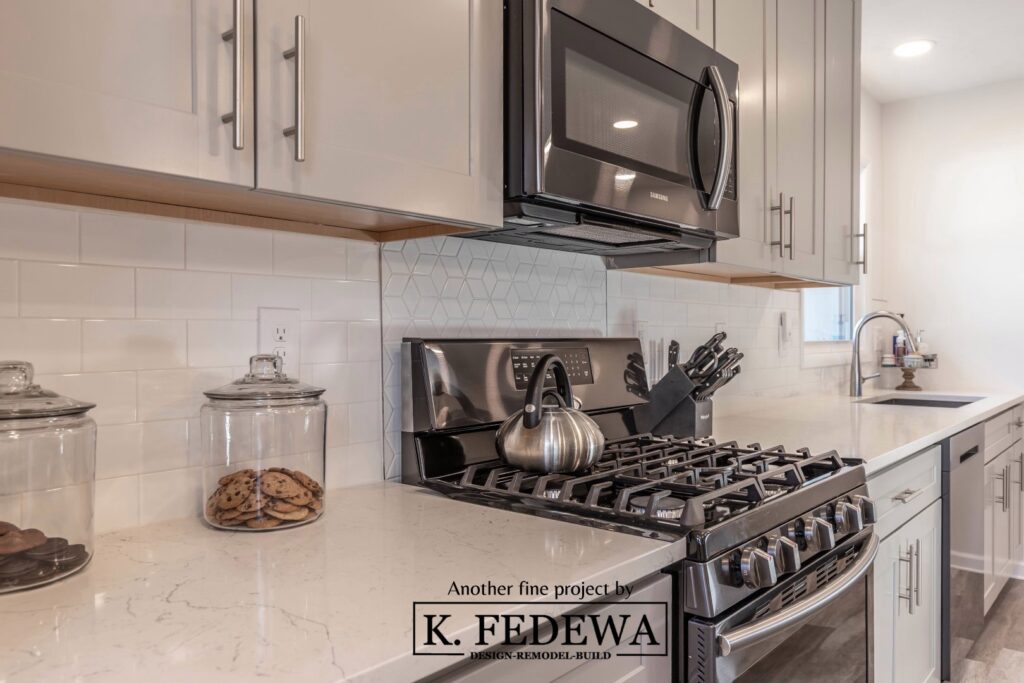 Close-up view of white Shaker style cabinets, white marble countertops, and stainless steel appliances.