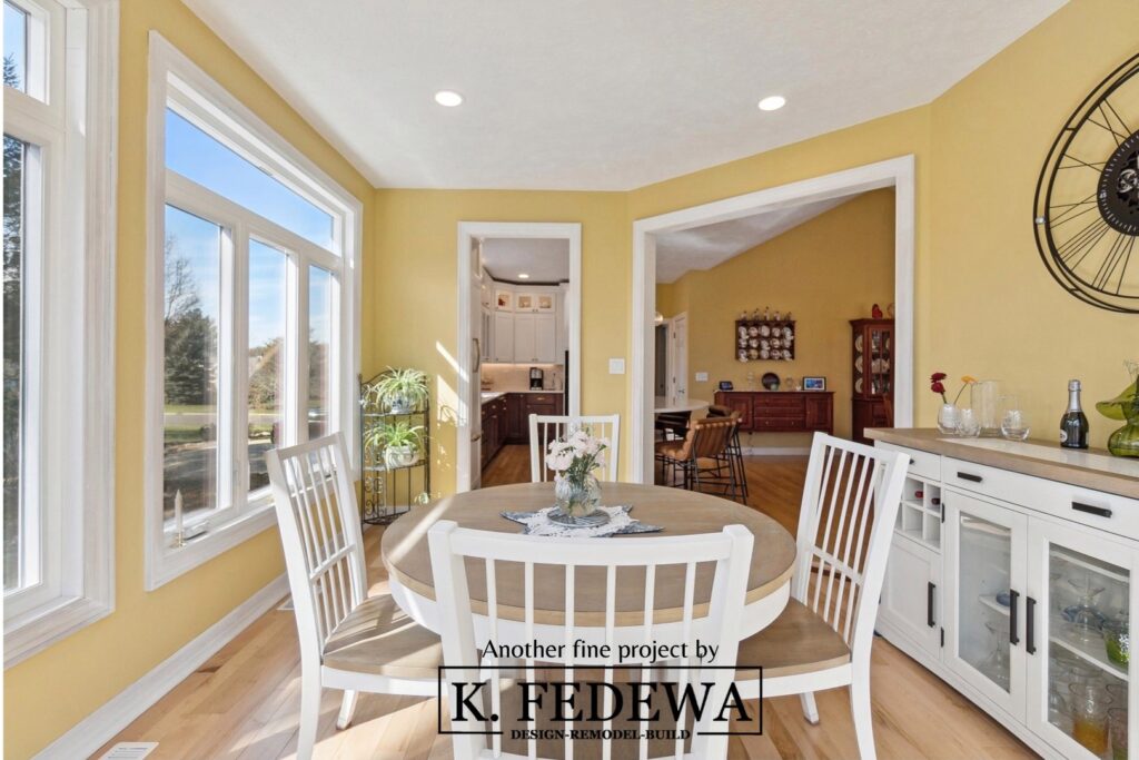 Beautiful four-seasons room in Bath, MI from K. Fedewa Builders with yellow walls and dining room set.