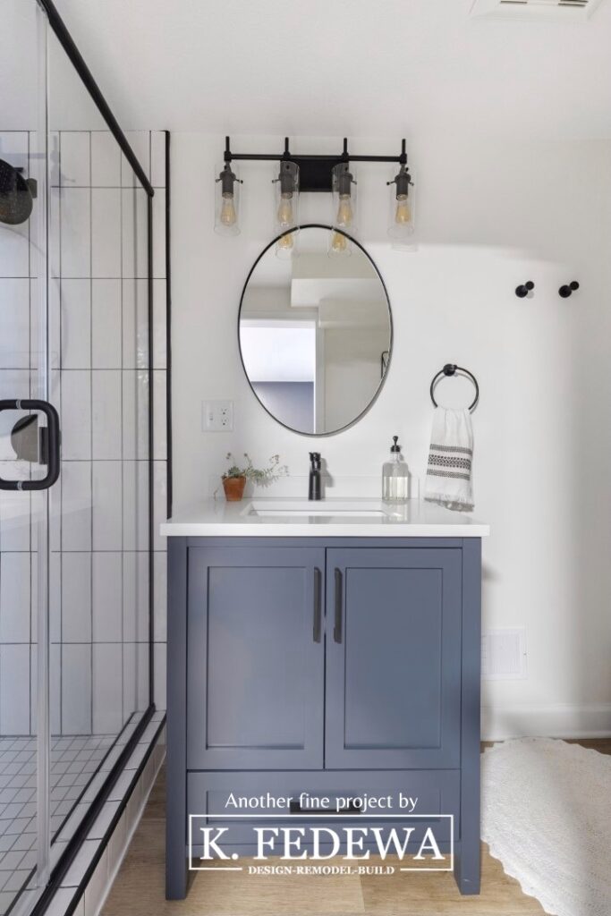 Beautiful blue bathroom vanity with white countertop with a black-rimmed oval mirror above it.