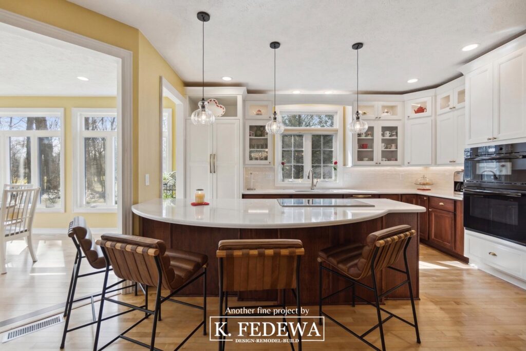 Huge curved island with stools in Bath, MI remodel with large white kitchen and sunroom entrance on the left-side.