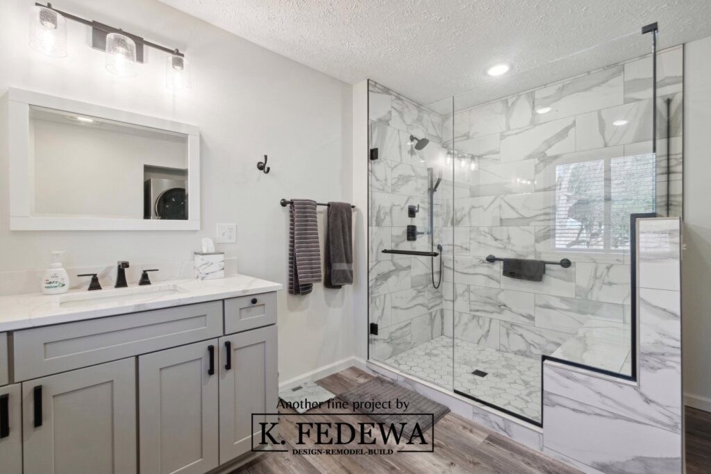 Gorgeous bathroom remodel with a grey vanity, wood flooring, and white and grey tiling.